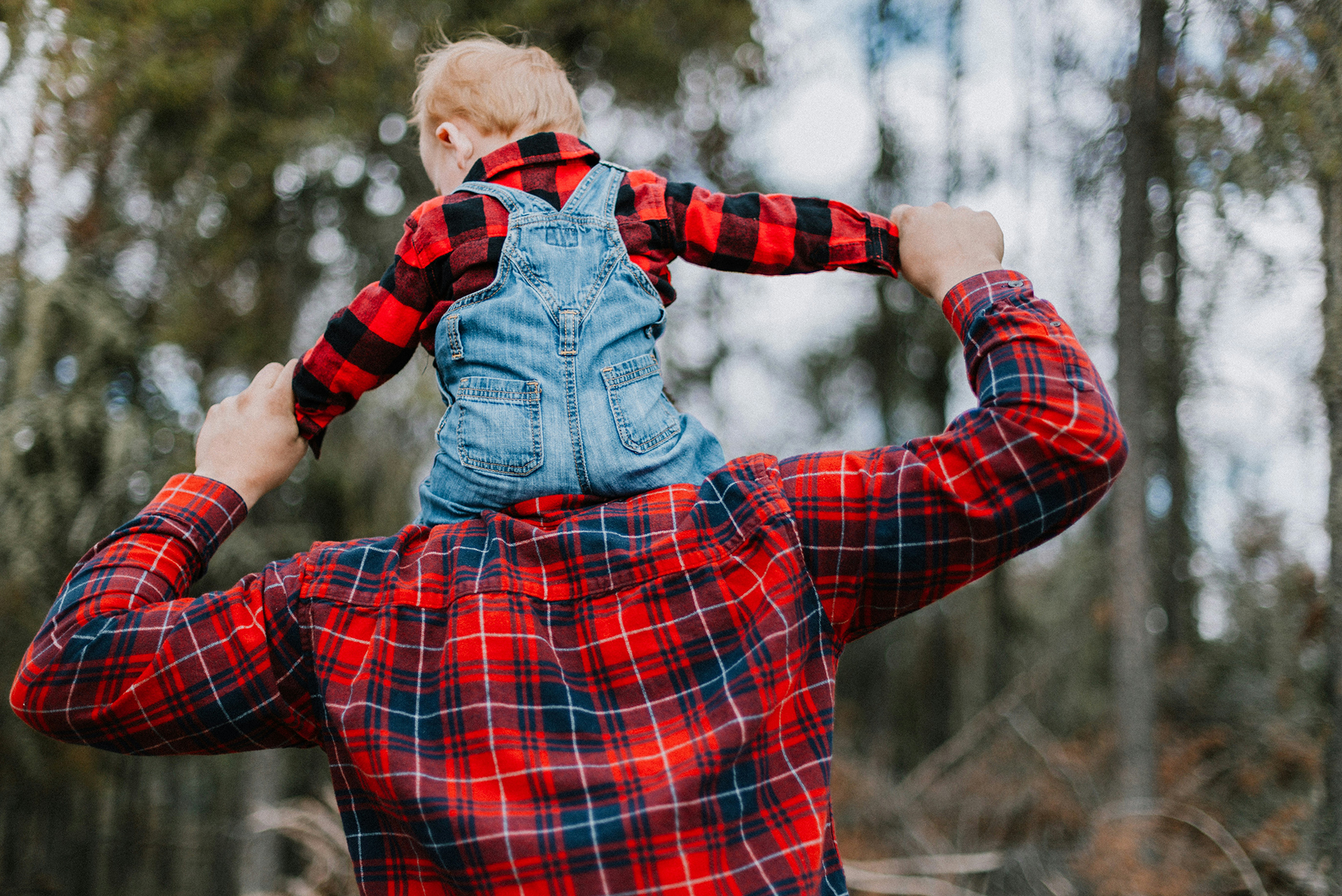 little kid sitting on father's shoulders, both wearing red flannel