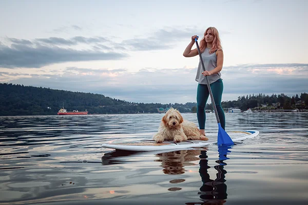 a young woman paddleboarding with her dog